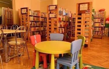 Kolorowy stolik i krzesełka dla dzieci stojące na dywanie w misie, za nimi regały z książkami