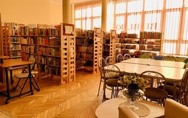 Po prawej stronie stoły z krzesłami, po lewej regały z książkami