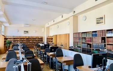 Na środku pomieszczenia trzy rzędy stolik&oacute;w z krzesłami, pod ścianami regały z książkami i czasopismami