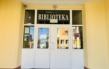 Białe  drzwi wejściowe, nad nimi biały napis Biblioteka