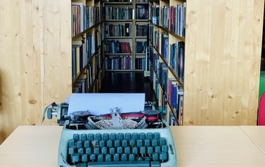 Stolik z maszyną do pisania, za nim widoczne regały z książkami