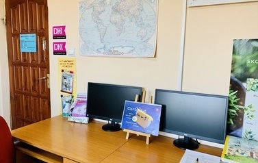 Dwa biurka z komputerami, nad nimi na ścianie mapa świata