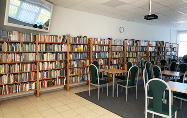Sala ze stolikami i krzesłami, w tle regały z książkami