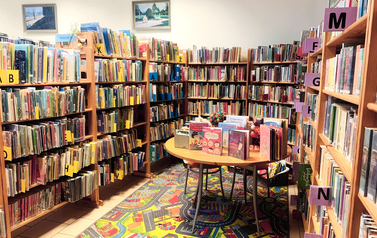 Sala z regałami z książkami, na środku kolorowy dywan i stolik z książkami