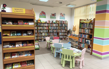 Sala z regałami z książkami, na środku kolorowe stoliki i krzesełka dla dzieci