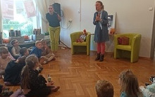 Kobieta stoi i mówi do dzieci siedzących na podłodze.
