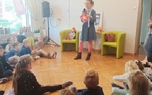 Kobieta stoi i mówi do siedzących przed nią dzieci.