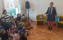 Kilkanaście osób siedzi na podłodze przed nimi kobieta.