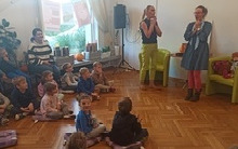 Kobieta stoi i mówi do dzieci siedzących na podłodze.