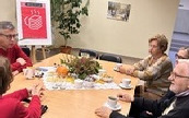 Kilkanaście osób siedzi na krzesłach i słucha osoby do nich mówiącej.