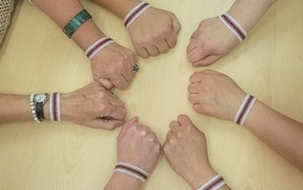 Siedem rąk ułożonych w koło i prezentujących na nadgarstkach bransoletki.