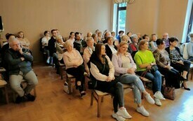 Grupa ludzi siedzi na krzesłach. 