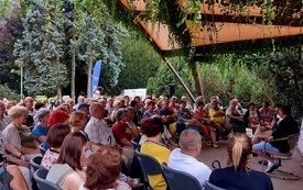 W parku siedzą uczestnicy spotkania. 