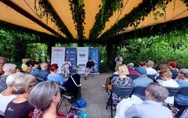 Pod zadaszeniem w parku siedzą uczestnicy spotkania autorskiego.