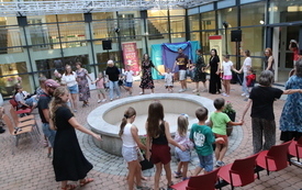 Wokół fontanny w kółku bawią się dzieci i rodzice.