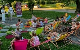 Na leżakach siedzą dzieci w otoczeniu natury.