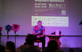 Pisarz z mikrofonem przy stoliku na scenie.