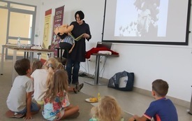 Pisarka z książką i maskotką przemawia do dzieci.