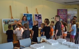 kobieta w okularach pokazuje dzieciom wystawę ilustracji.