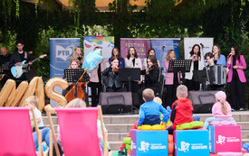 Koncert zespołu na scenie. Przed nia siedzą dzieci. 