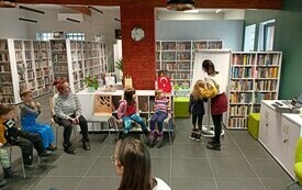 Grupa dzieci siedzi na krzesłach pomiędzy regałami z książkami
