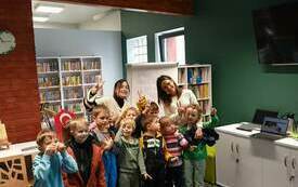 Grupa dzieci pozujących na stojąco do zdjęcia, za nimi regały z książkami