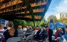 Pod zadaszeniem w parku siedzą uczestnicy spotkania.