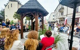 Widok na studnię miejską przy której siedzą zaproszeni goście.