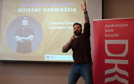 Młody mężczyzna z mikrofonem wskazuje ręką na sufit