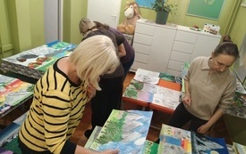 Cztery kobiety stoją w sali pełnej prac plastycznych rozłożonych na stolikach
