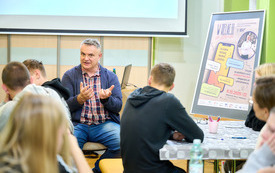 Prowadzący spotkanie mężczyzna m&oacute;wi do zebranej młodzieży. 