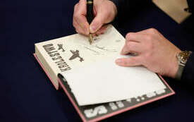 Dłonie pisarza podpisującego książkę.