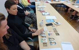 Kobieta w czarnym ubraniu patrzy na leżące na stoliku zdjęcia portretowe r&oacute;żnych os&oacute;b.