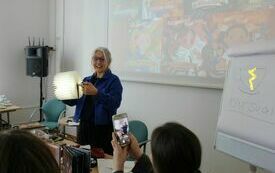 Kobieta w okularach trzyma w ręku lampę wyglądającą jakby była zrobiona z kartek 