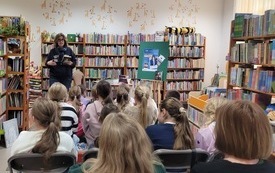 Kobieta w średnim wieku z książką prowadzi spotkanie dla dzieci. 