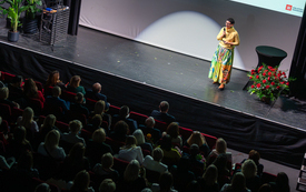 Widok z teatralnego balkonu na publiczność i kobietę przemawiającą na scenie