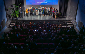 Widok z balkonu teatru na publiczność oraz grupę nagrodzonych bibliotekarzy stojącą na scenie