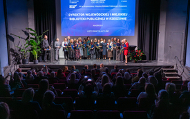 Grupa nagrodzonych bibliotekarzy pozuje do wsp&oacute;lnego zdjęcia na scenie