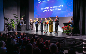 Cztery kobiety pozują na scenie do wsp&oacute;lnego zdjęcia trzymając w dłoniach kwiaty i prezenty