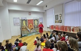 Kobieta w czerwonej sukience przemawia do zebranej publiczności.