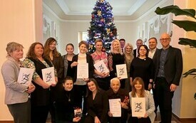 Grupa os&oacute;b z dyplomami na tle choinki. 