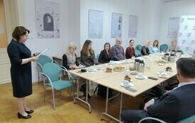 Przy dużym stole konferencyjnym siedzą bibliotekarze, z boku stoi dyrektorka i przemawia. 