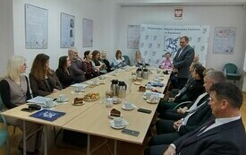 Kilkanaście os&oacute;b przy stole konferencyjnym. 