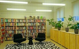 Widok wnętrza biblioteki, na pierwszym planie stolik i dwa fotele, za nimi p&oacute;łki z książkami