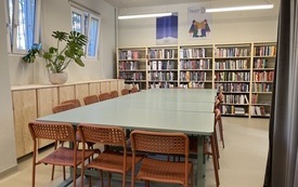 Duży st&oacute;ł z krzesłami, w tle regały z książkami.