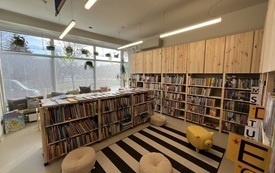 Dywan w paski, na dywanie pufy do siedzenia, obok regały z książkami.