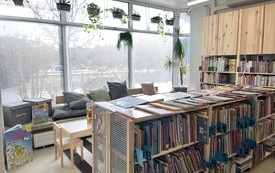 Regały z książkami, na parapetach miejsce z poduszkami do siedzenia, powyżej kwiaty