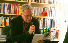 Mężczyzna czyta na głos z otwartej książki, kt&oacute;rą trzyma w dłoniach