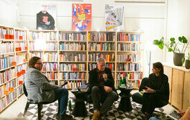 Dwaj mężczyźni i kobieta siedzą na tle regał&oacute;w z książkami