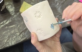 Kobiece ręce malujące gliniany kubek w kwiaty